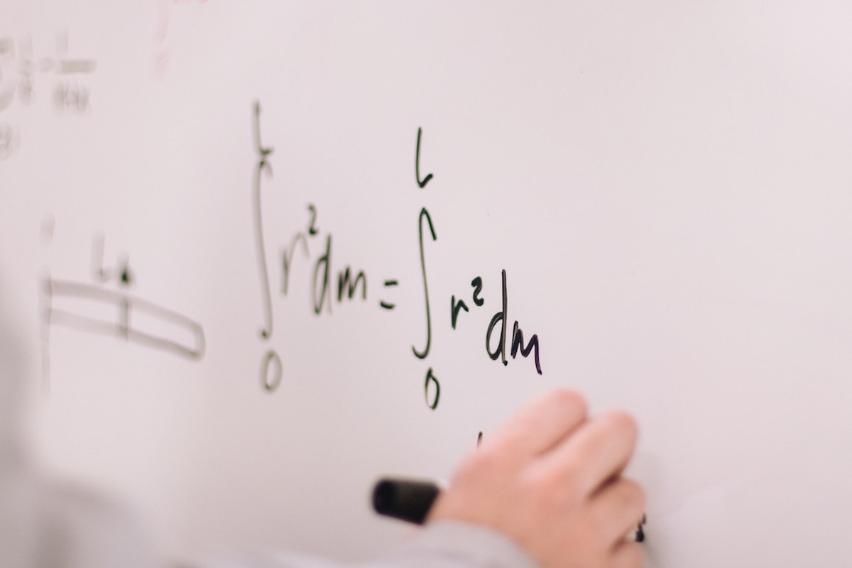 Uma mão fazendo fórmulas matemáticas em um quadro branco