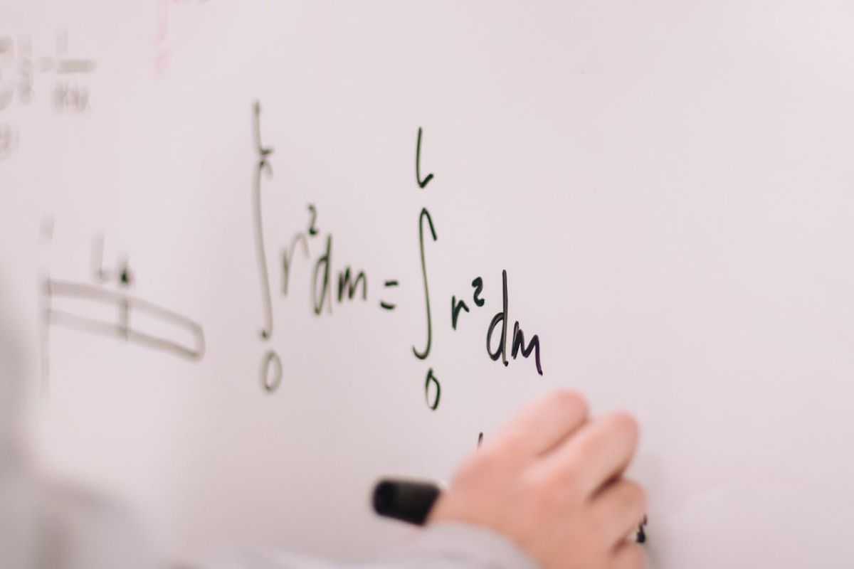 Um professor escreve algumas fórmulas matemáticas em um quadro branco com uma caneta preta