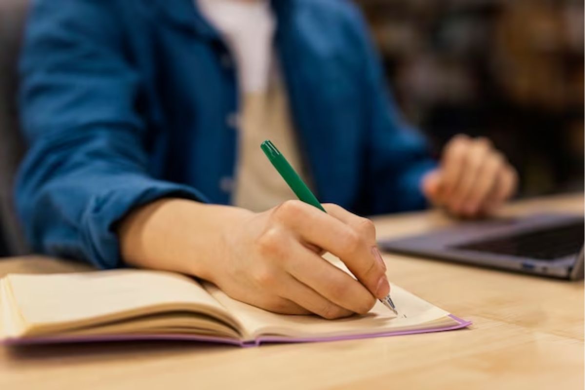 Um aluno está sentado enquanto escreve no caderno.