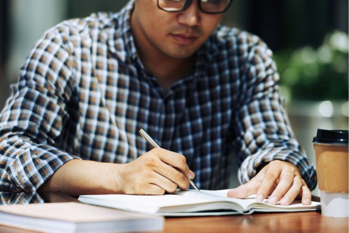 Um aluno está sentado enquanto escreve no caderno.