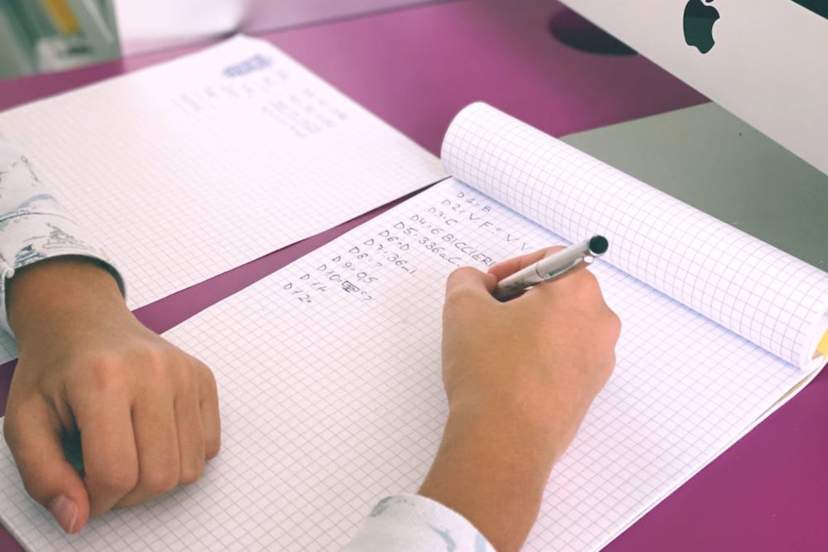 Uma aluno do SENAI Itatiba 2024 está fazendo anotações em um caderno utilizando uma caneta