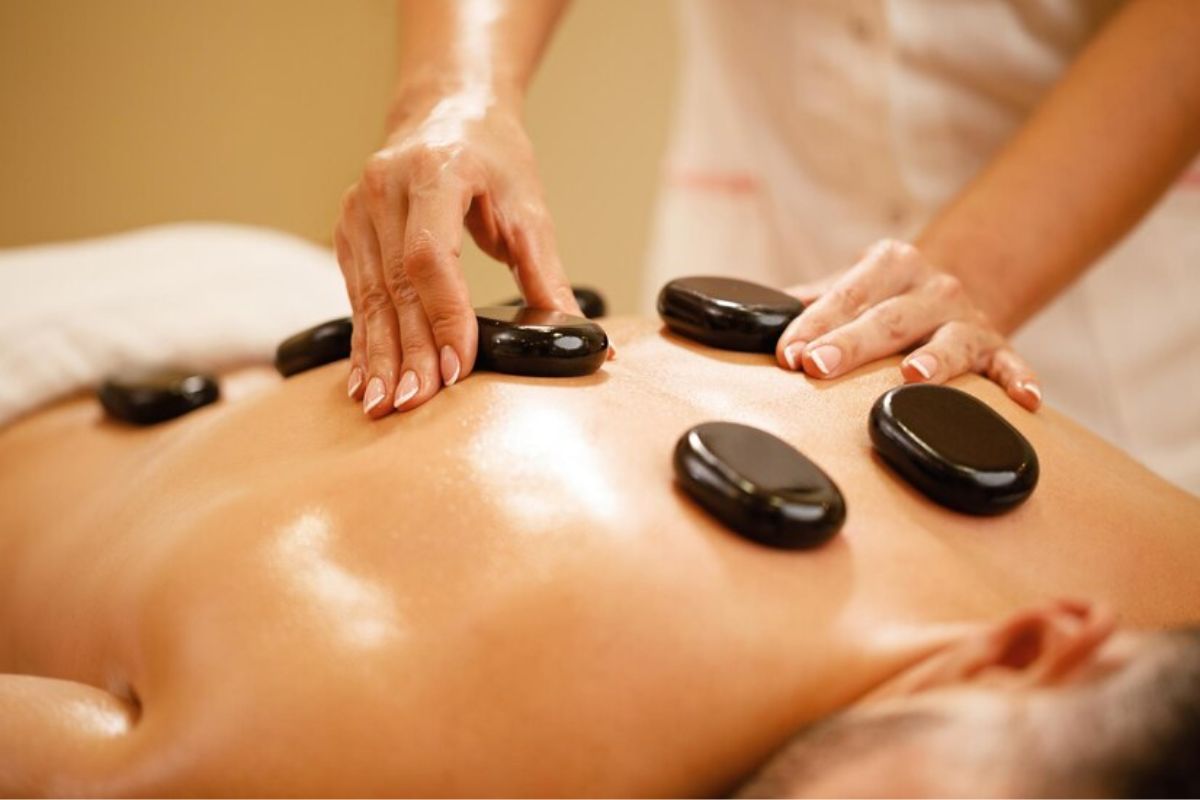 Imagem de pedras de spa em cima das costas de um homem que está recebendo massagem