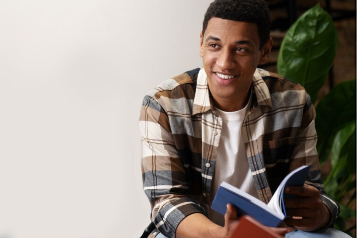 Um aluno está sentada com um caderno na mão sorrindo
