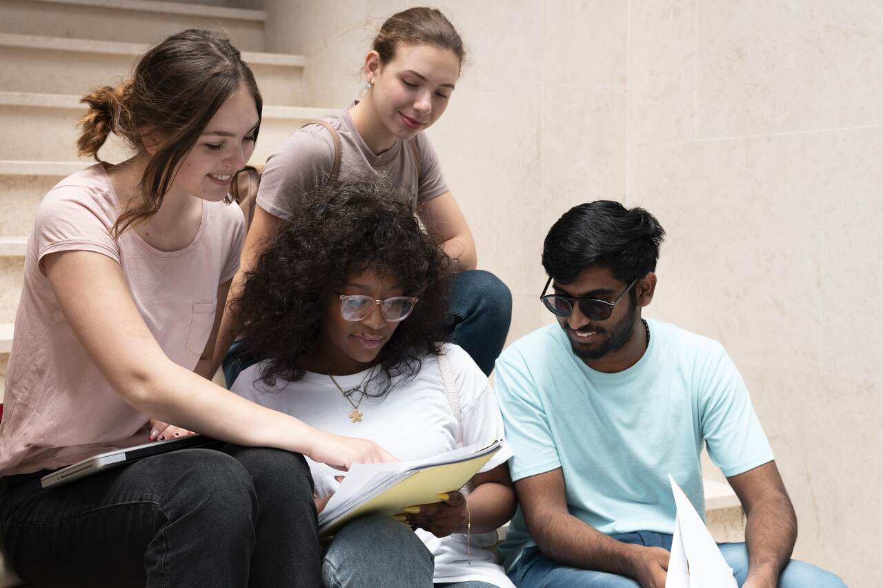 Grupo de estudantes sentados em escada com cadernos estudando 