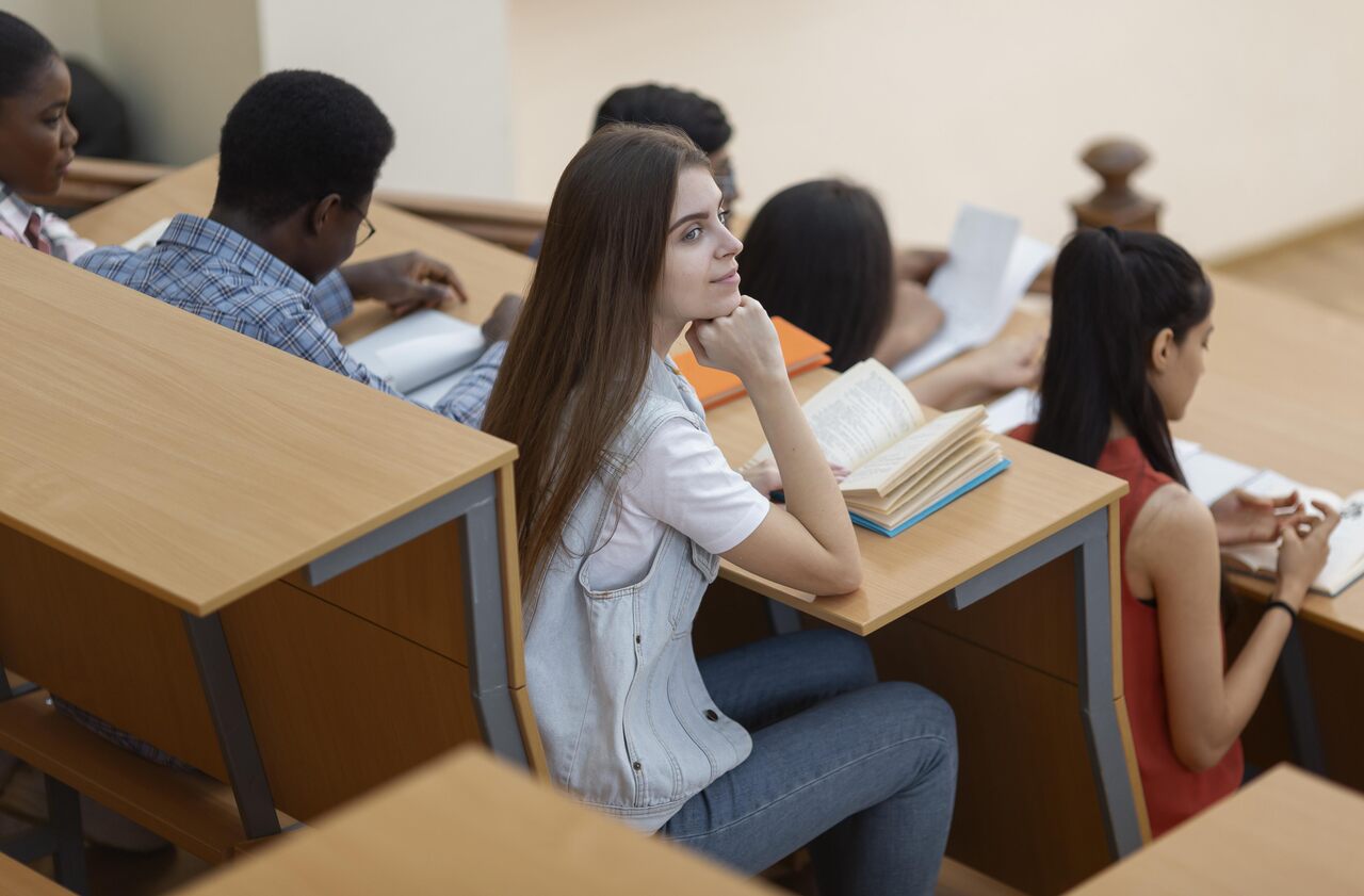 Estudantes sentados em carteiras em sala de aula com cadernos e lápis 