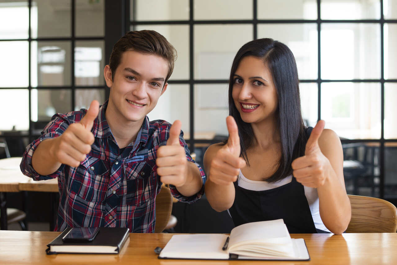 Estudantes animados fazem sinal de positivo com polegar para cima 