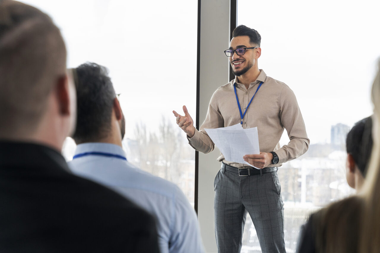 Jovem faz apresentação para grupo de pessoas em ambiente corporativo 