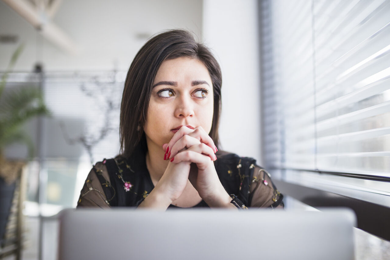 Mulher sentada diante o notebook com expressão pensativa 