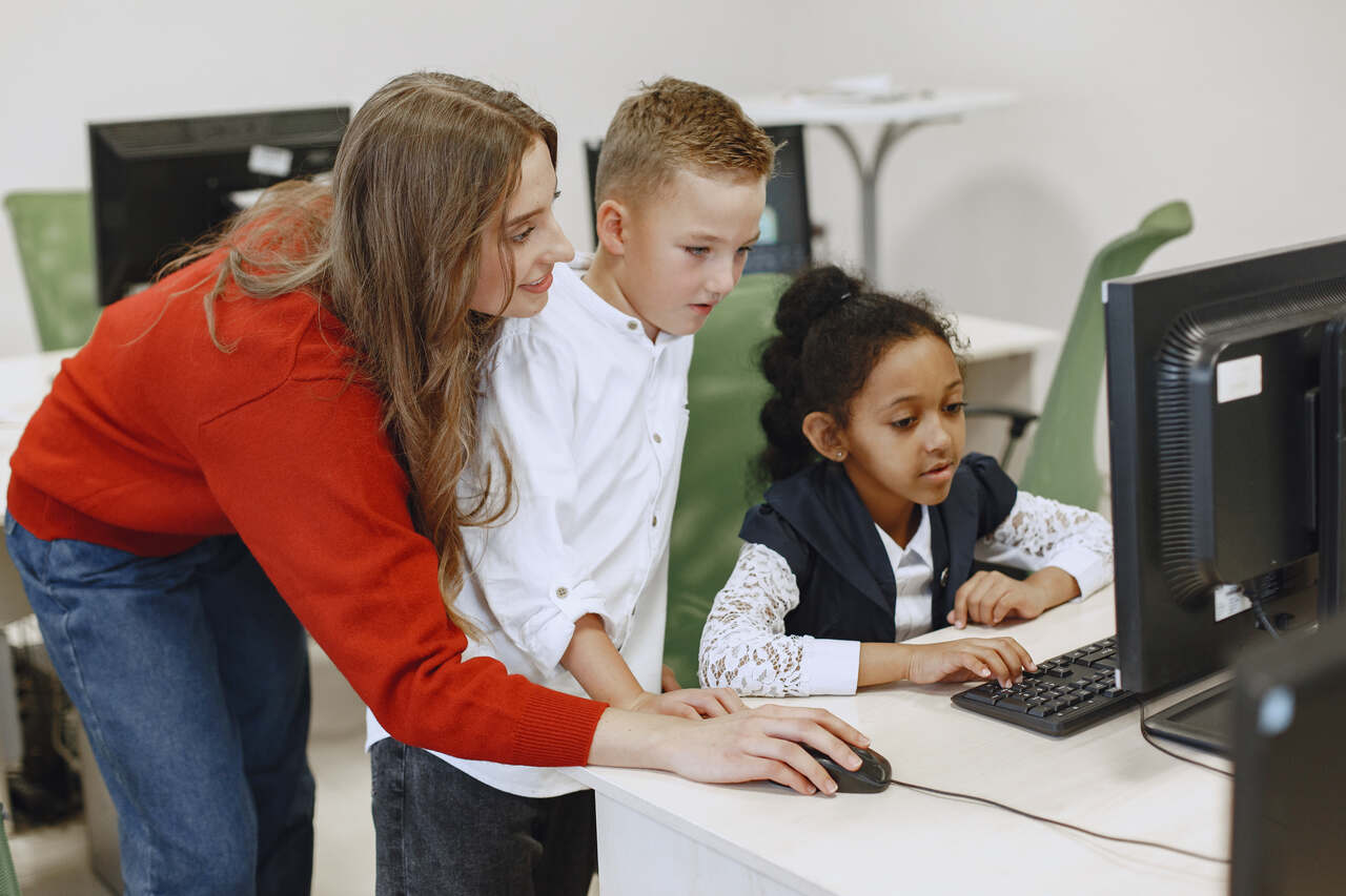 Professora auxilia alunos em aula no laboratório de informática 