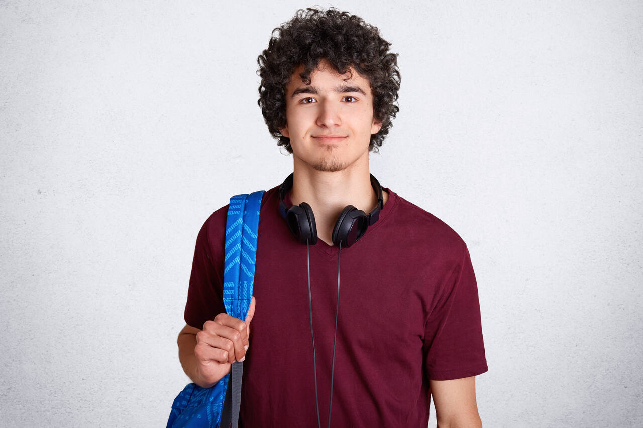 Jovem estudante posa sorrindo carregando mochila no ombro